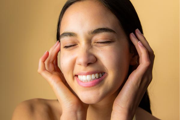 Image of model smiling with a full face of Cotz Face Moisture Lightly Tinted SPF 35 to show off the velvety finish of the product