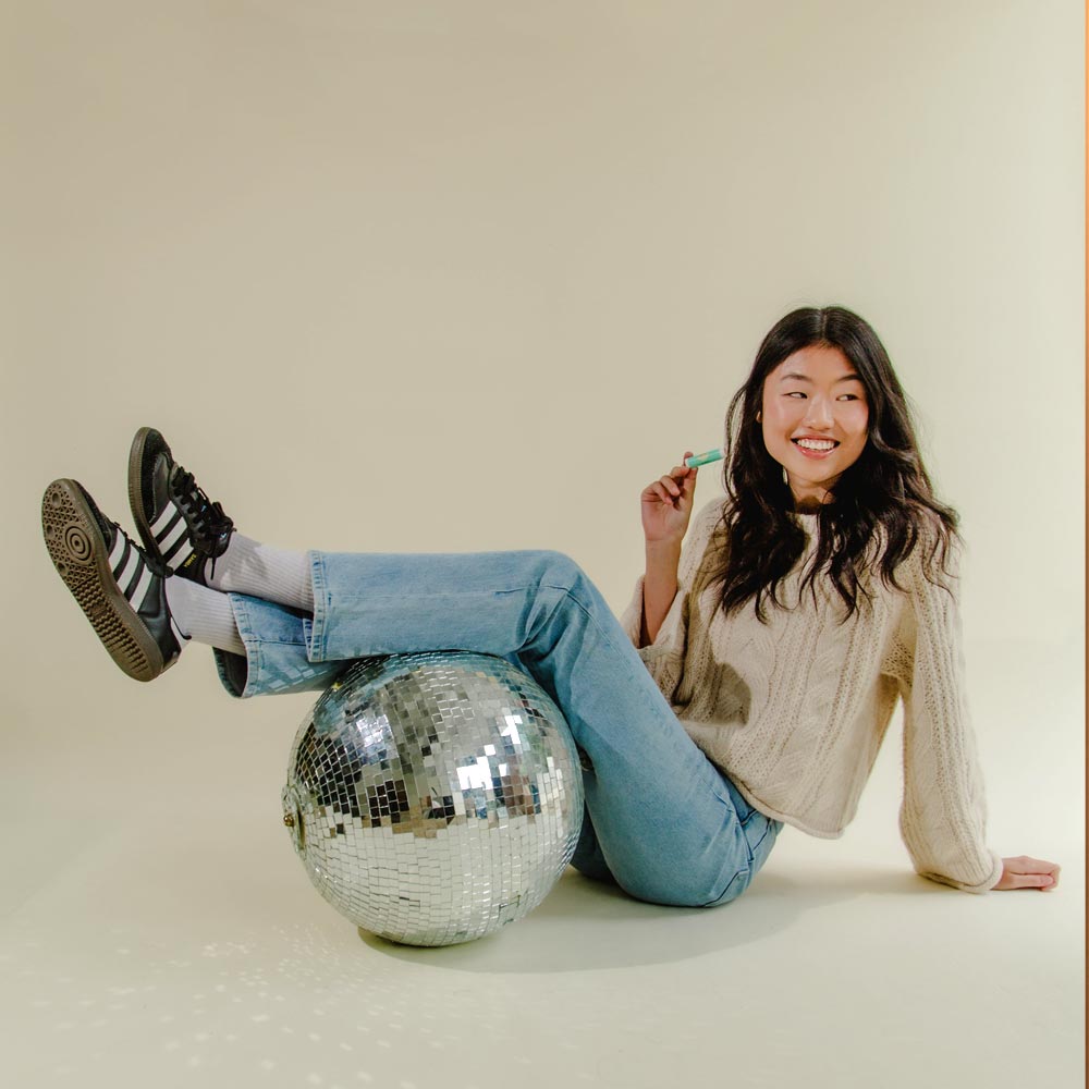 Image of model with feet propped up on disco ball holding Cotz Lip Balm Tinted SPF 45