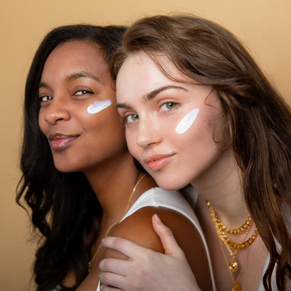 Image of two models back to back with Cotz Sensitive Non-Tinted SPF 40 swatches on their cheeks