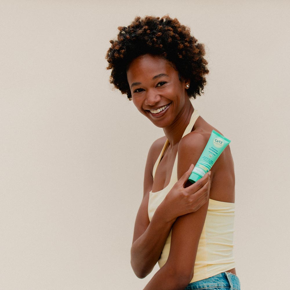 Image of model holding Cotz Flawless Complexion Richly Tinted SPF 50 near her shoulder while smiling