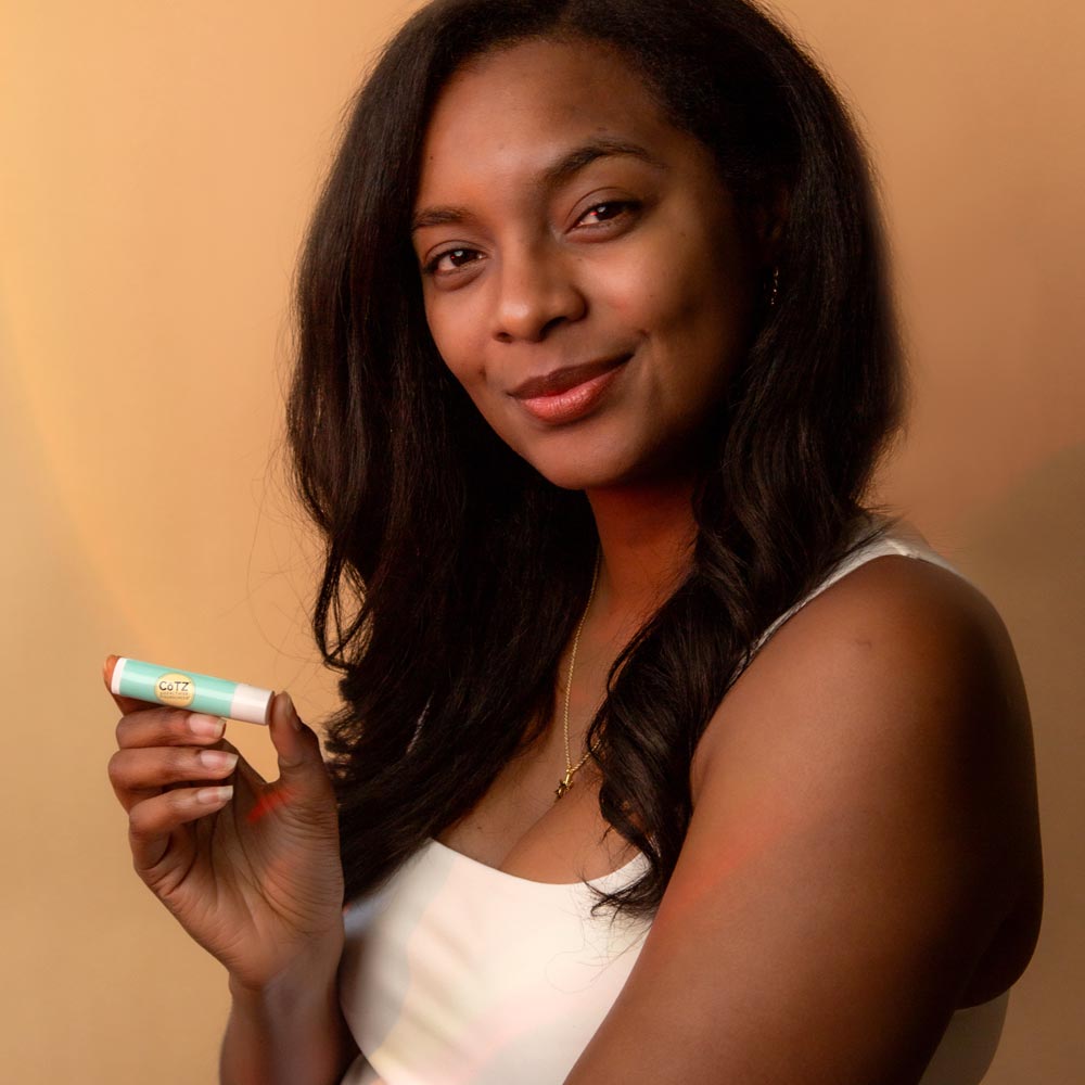 Image of model holding Cotz Lip Balm Tinted SPF 45 while smiling 