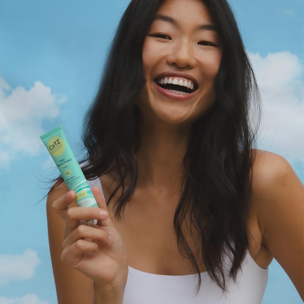 Image of model holding Cotz Face Prime & Protect Tinted SPF 40 tube with sky in the background