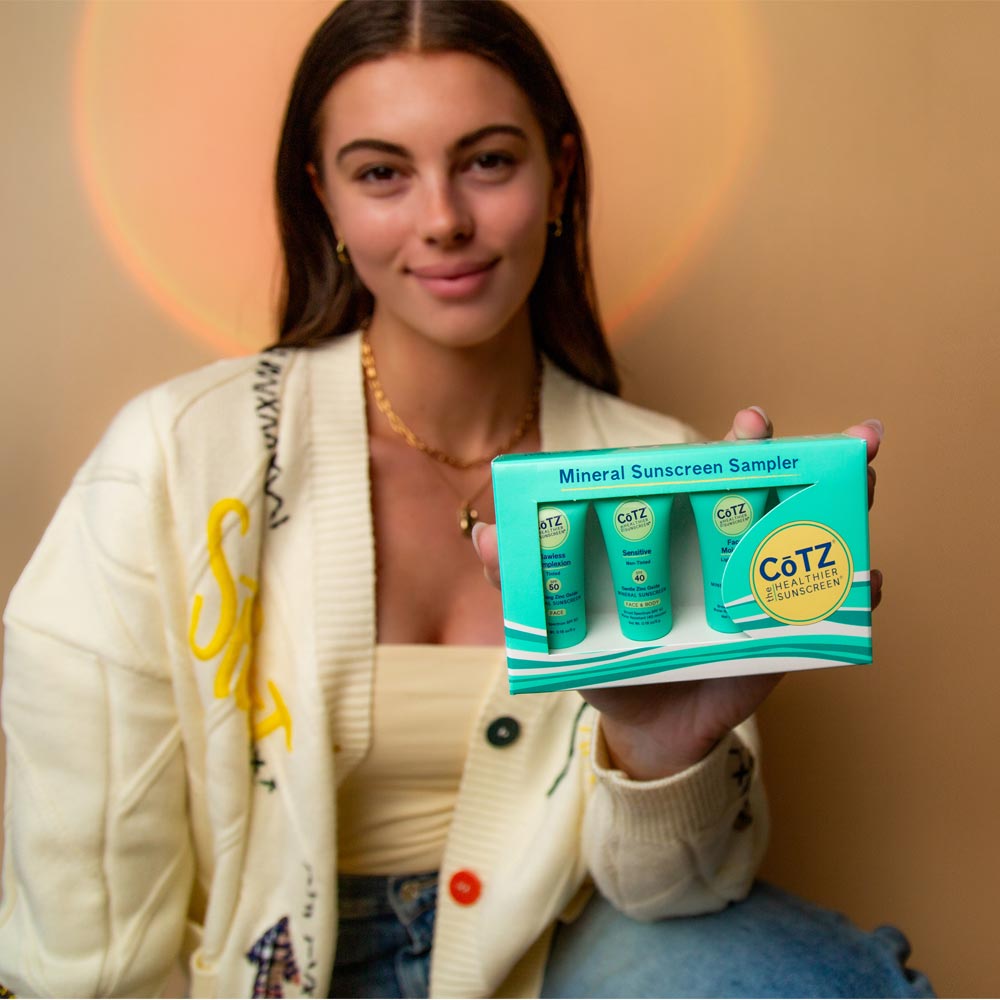 Image of model holding Cotz Mineral Sunscreen Sampler in box while smiling