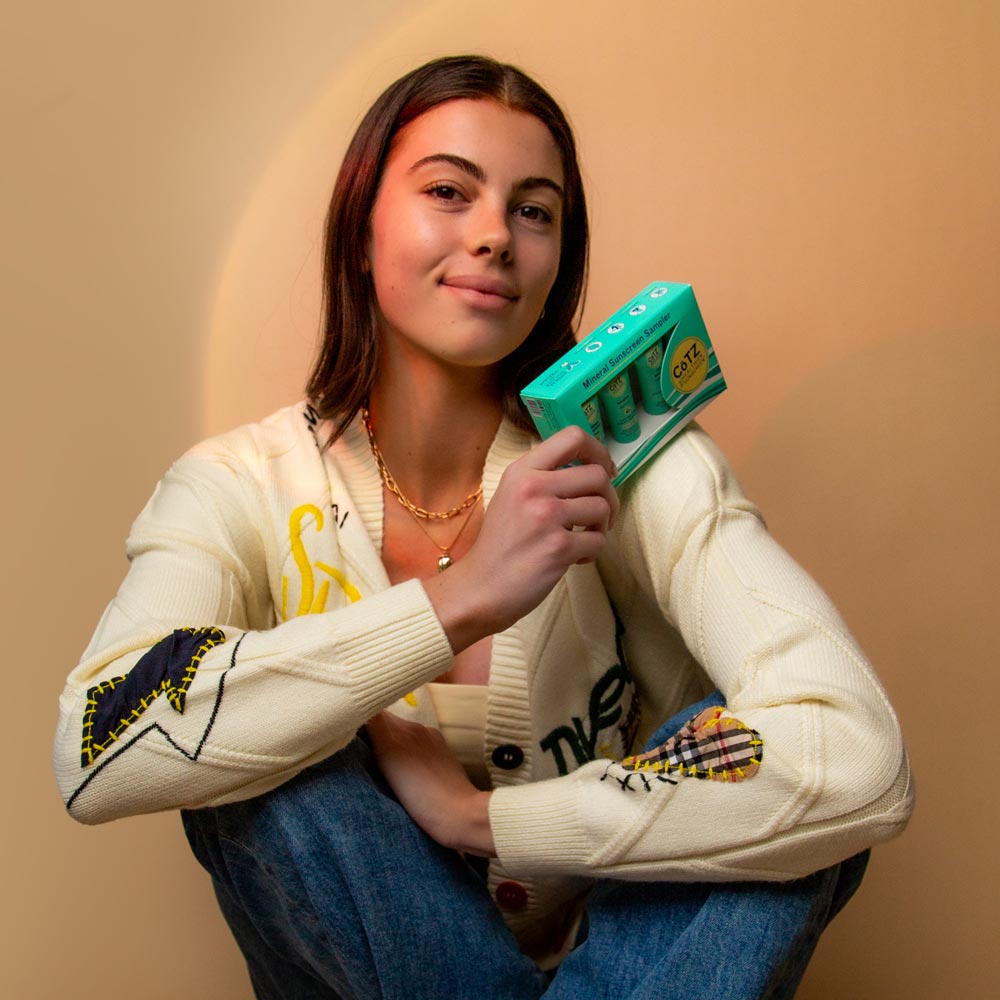 Image of model holding Cotz Mineral Sunscreen Sampler box on her shoulder smiling