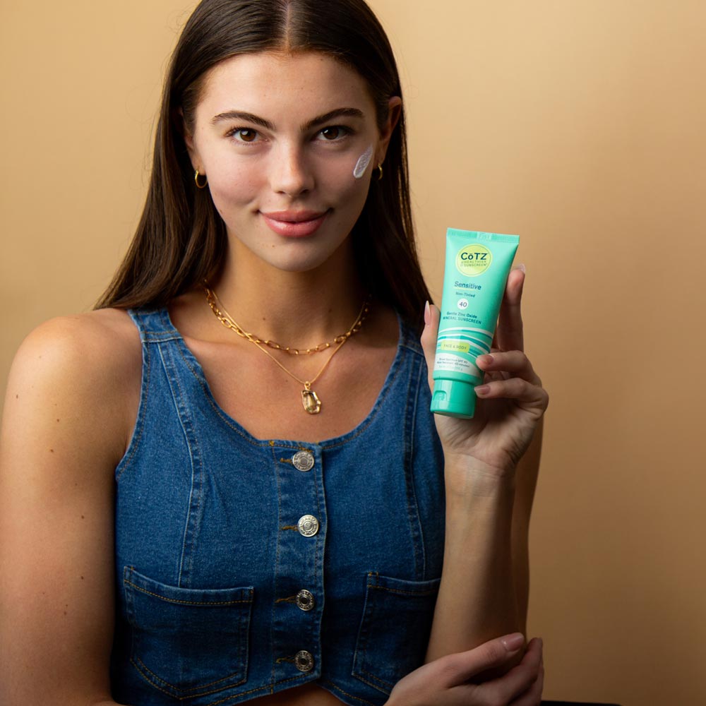 Model holding Cotz Sensitive Non-Tinted SPF 40 tube with sensitive swatch on her cheek 