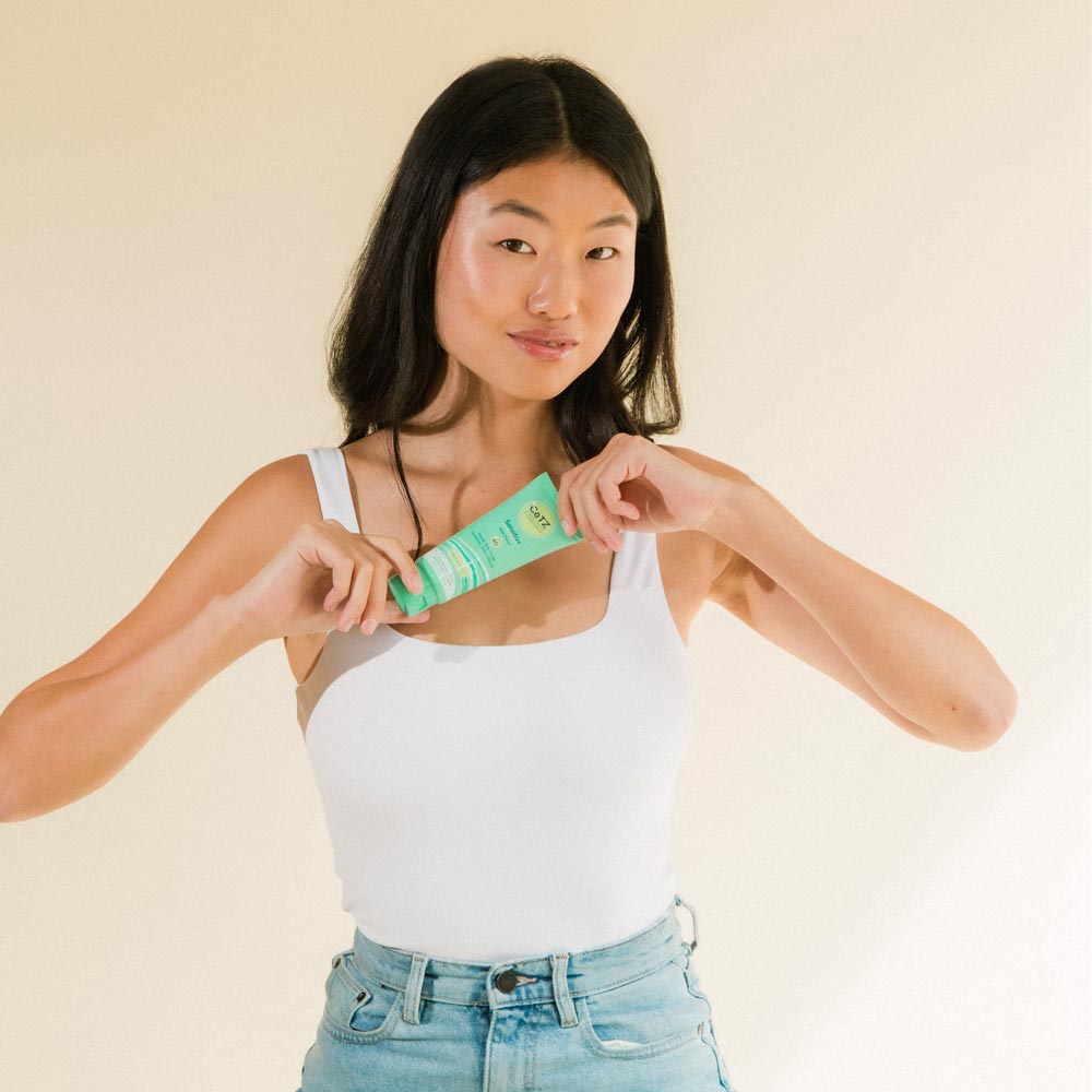 Model holding Cotz Sensitive Non-Tinted SPF 40 near her chest while smiling