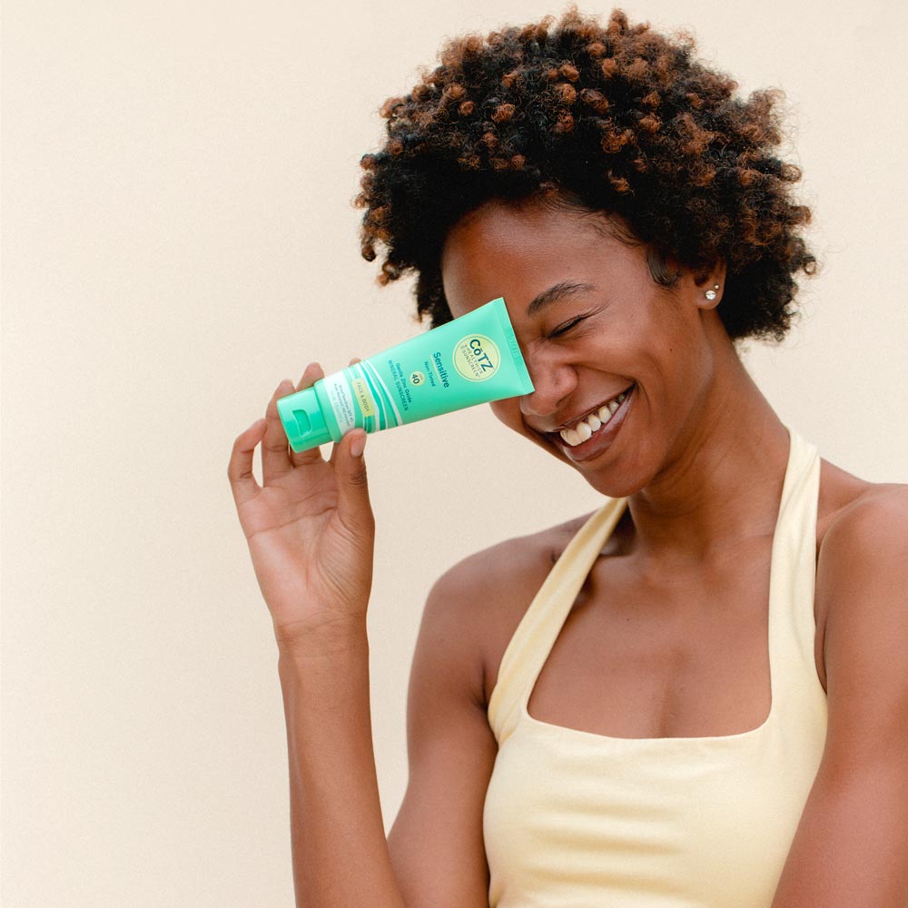 Model holding Cotz Sensitive Non-Tinted SPF 40 tube near face while laughing