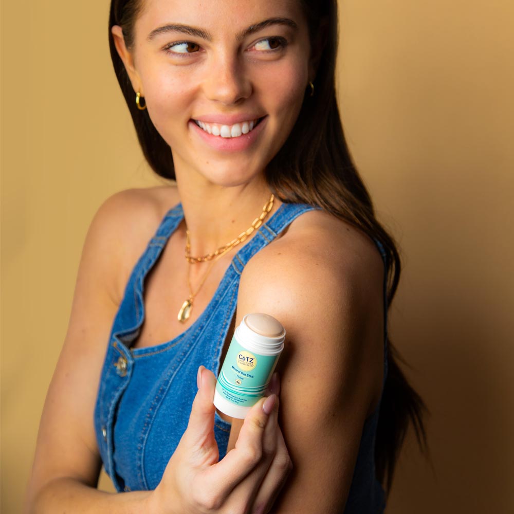 Model looking off to the side holding Cotz Mineral Sun Stick Tinted SPF 45 near her shoulder