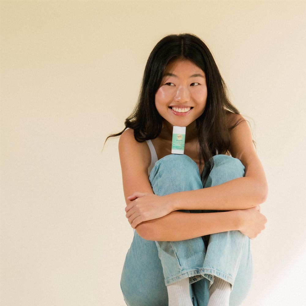 Model smiling and sitting with Cotz Mineral Sun Stick Tinted SPF 45 in between her chin an knee